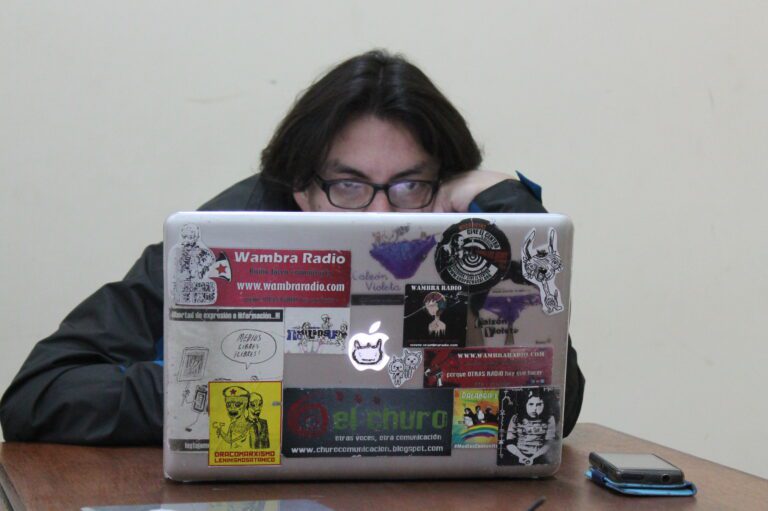 Eine Person sitzt hinter einem aufgeklappten Laptop, der mit Aufklebern übersät ist.